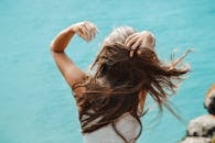 Back view of a woman with flowing hair near the sea in Portugal, capturing a moment of solitude.